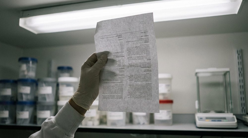 Lab technician in white gloves holding a densely printed construction chemicals datasheet up to fluorescent lighting — reading between the rows