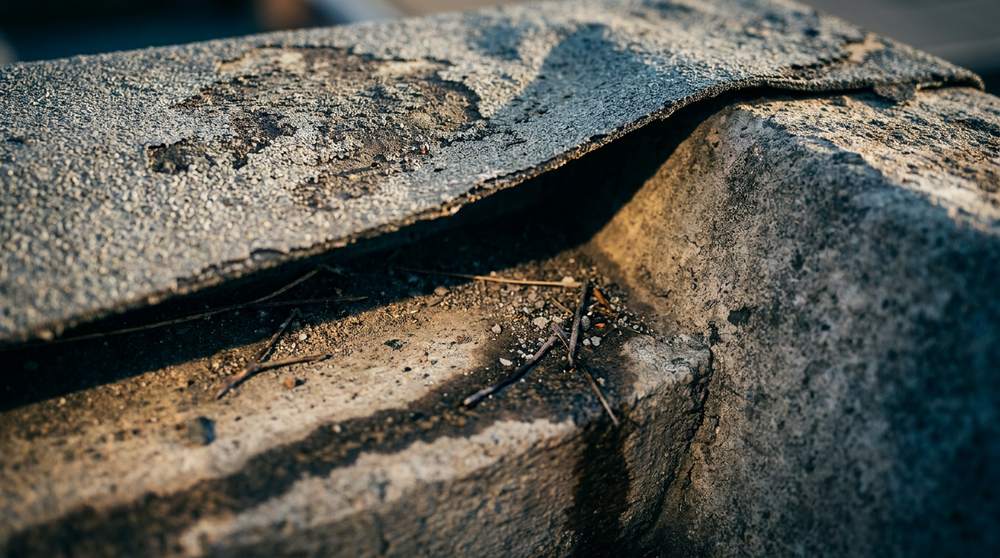 Macro detail of lifted membrane seam at flat roof interface — debonding failure mode at singularity